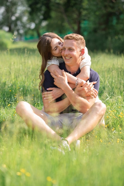 Милая молодая пара сидит на траве и целует молодого мужчину и женщину, наслаждаясь летним днем счастливые люди в л