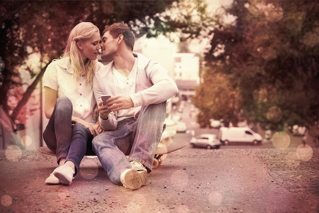 Cute young couple sitting on skateboard kissing on a sunny day in the city