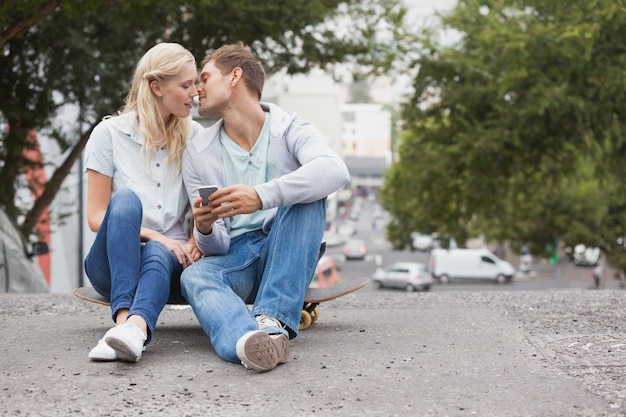 スケートボードに座っているキュートな若いカップルキス