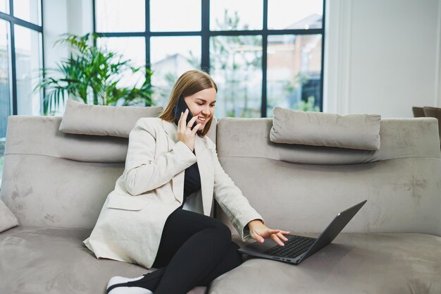 Cute young freelancer woman in casual clothes relaxing on sofa while working on internet via netbook while remote working on project at home