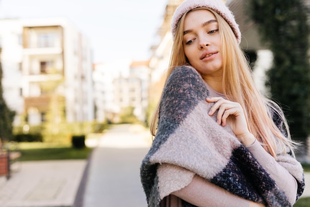 Cute young girl blond model in hat, on shoulders warm scarf, walking outdoors