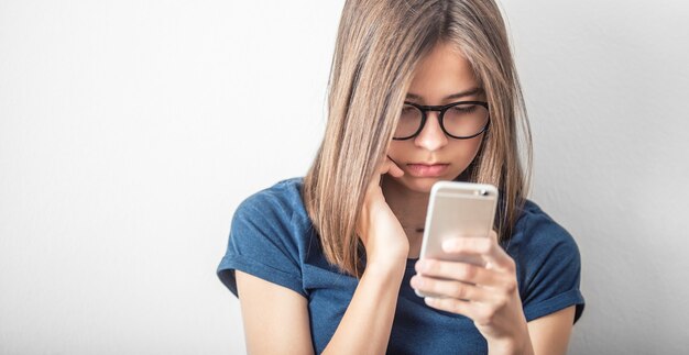 Foto la ragazza sveglia in camicia blu legge il messaggio o il video al telefono cellulare.