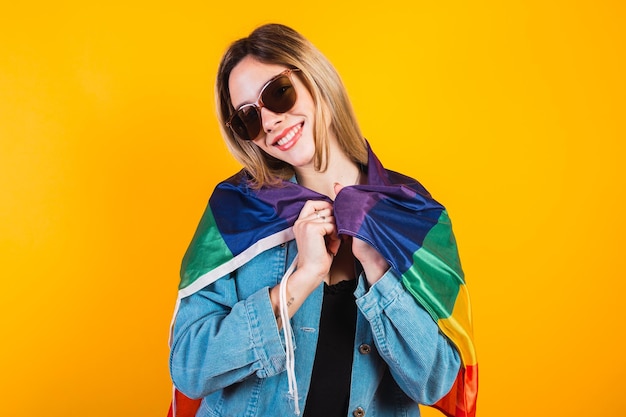 Photo cute young girl drapes herself with large rainbow flag on yellow background.