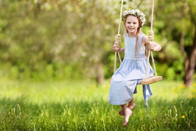 Cute young girl  having fun on a swing in blossoming old apple tree garden. Sunny day. Spring outdoor activities for kids