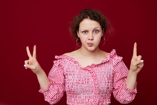 Фото Симпатичная молодая девушка в розовой рубашке жестикулирует руками на красном фоне студии без изменений