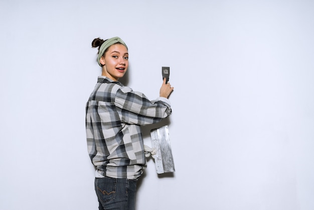 Cute young girl in a plaid shirt doing repairs in her apartment, leveling the walls with a spatula