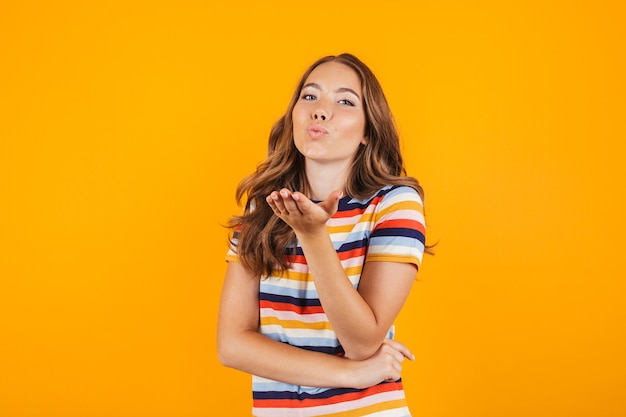 Cute young girl posing over yellow wall space blowing kisses.