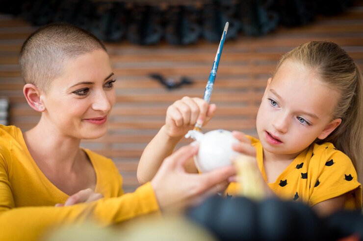 Photo cute young girl sitting at a table decorating little pumpkins with her mother a cancer patient