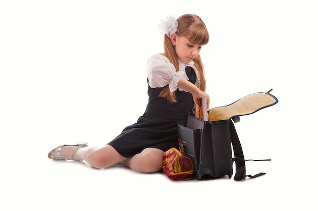 Cute young girl in uniform parking school bag; isolated on white 