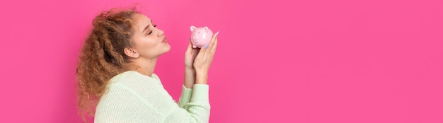 A cute young girl with curly red hair holds a piggy bank a pink piglet in her hands The concept of wealth and safety of money