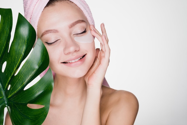 Photo cute young girl with a pink towel on her head enjoying a spa, under eyes patches