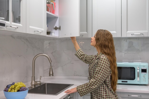 Cute young housewife opens the kitchen cabinet door