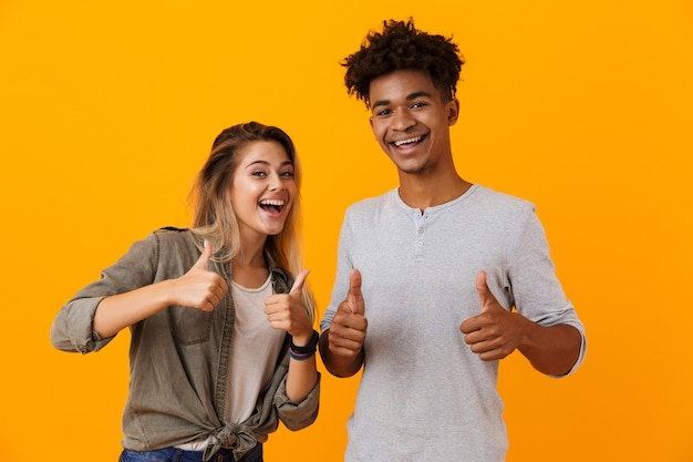 Cute young loving couple posing isolated over yellow wall showing thumbs up