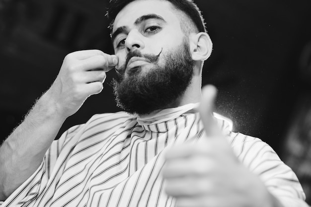 Cute young man with beautiful mustache and beard sitting in an armchair in barbershop