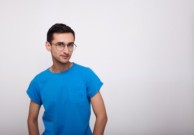 A cute young man with glasses and a blue T-shirt looks straight.