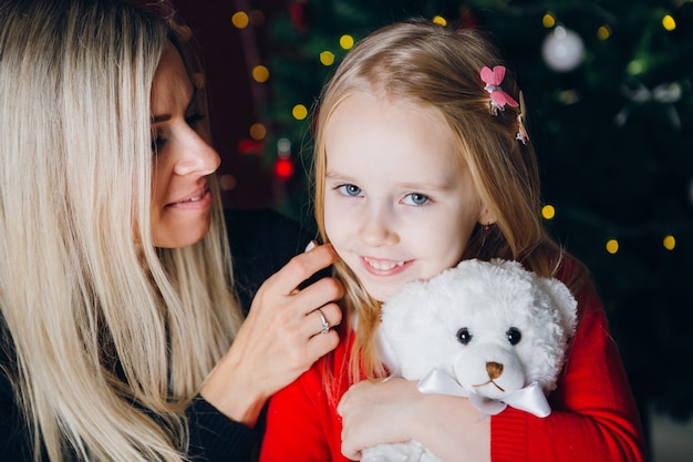 Cute young mother with blonde hair and a little daughter are sitting on a chair