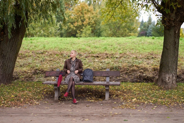 写真 ベンチに座って、秋の公園でリラックスしてかわいい若い短い髪のブロンドの女性