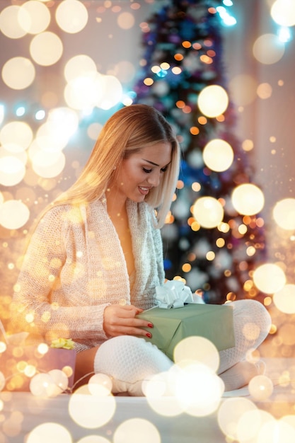 Cute young smiling woman is holding gift surrounded with Christmas bubble lights.