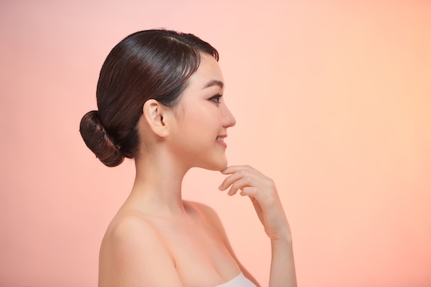 Cute young smiling woman touches her clean skin, on biege background