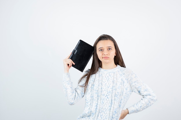 cute young student posing with notebook on white wall.