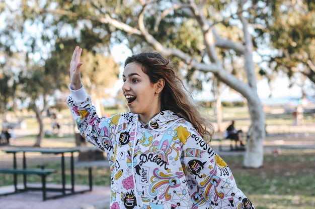 Cute young teenager girl greeting friends outdoors. School girl waving hand to her friends