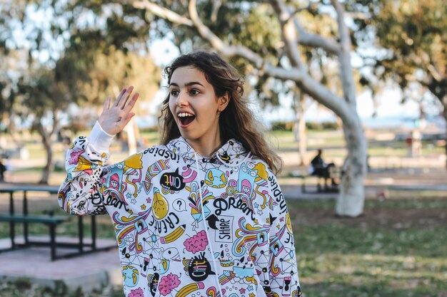 Cute young teenager girl greeting friends outdoors. School girl waving hand to her friends