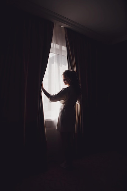 Cute young woman bride in home bathrobe at window in hotel room