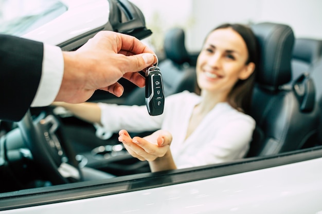 Cute young woman buying a new car for job and travel in dealership girl customer with salesman