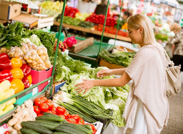 かわいい若い女性が市場で野菜を買う