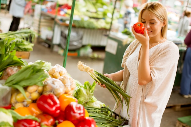 かわいい若い女性が市場で野菜を買う