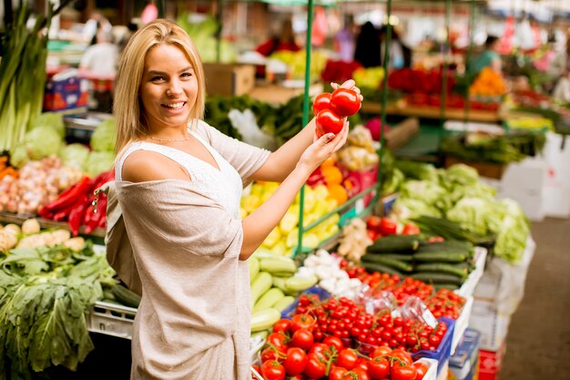 かわいい若い女性が市場で野菜を買う