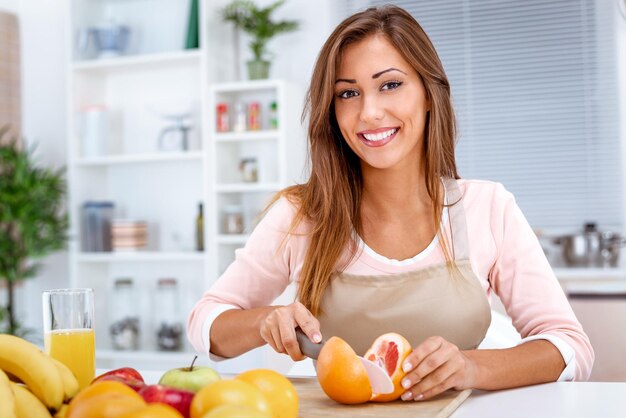 Cute young woman cutting grapefruit in kitchen.