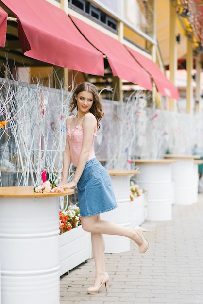 Photo cute young woman in a denim skirt and pink top stands near a metal