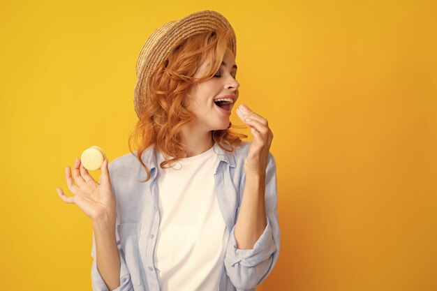 Cute young woman hold macaroon beautiful smiling young girl eating colorful macaroons over yellow background