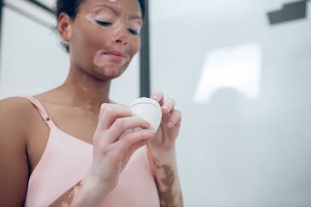 A cute young woman holding a jar of face cream in hands