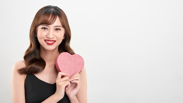 Cute young woman holding pink heart symbol against pale white background