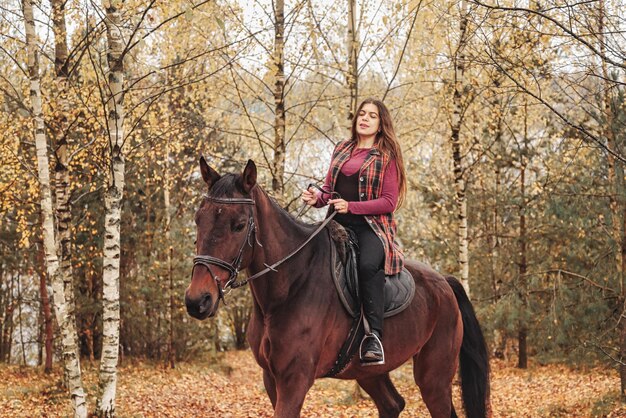 Cute young woman on horseback in autumn forest