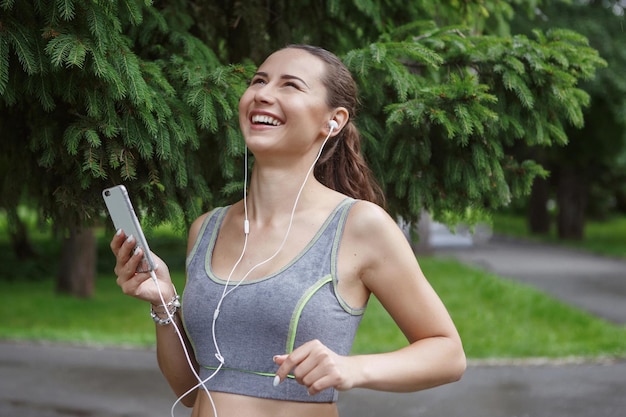 Cute Young woman listening to music while jogging down the path in a green park