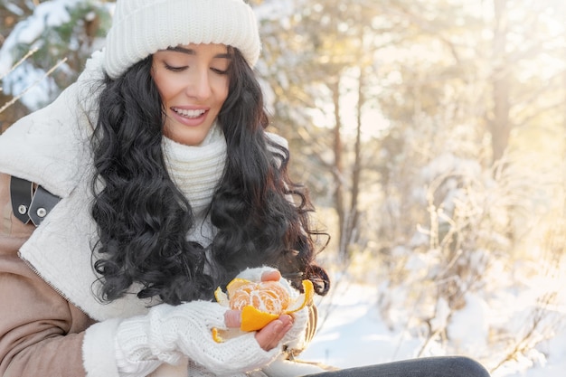 Cute young woman peels tangerine in winter fairy forest, Christmas or new year holidays concept