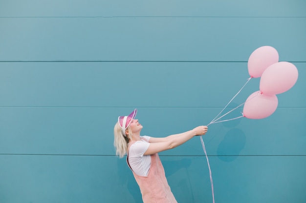 Cute young woman in pink clothes standing with balloons