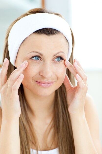 Photo cute young woman putting cream on her face in the bathroom