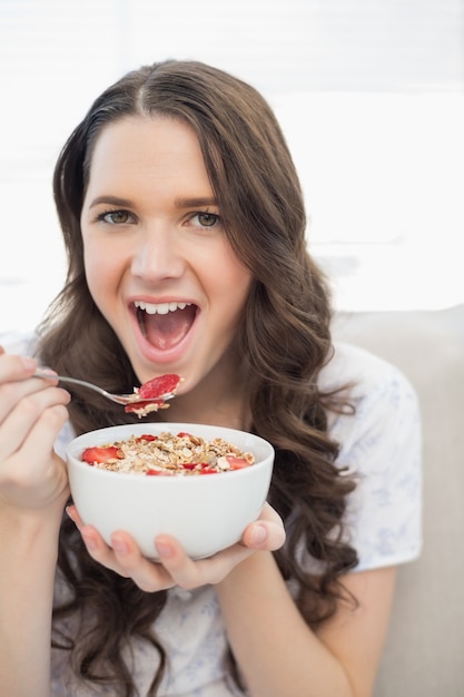 Cute young woman in pyjamas eating fruity cereal