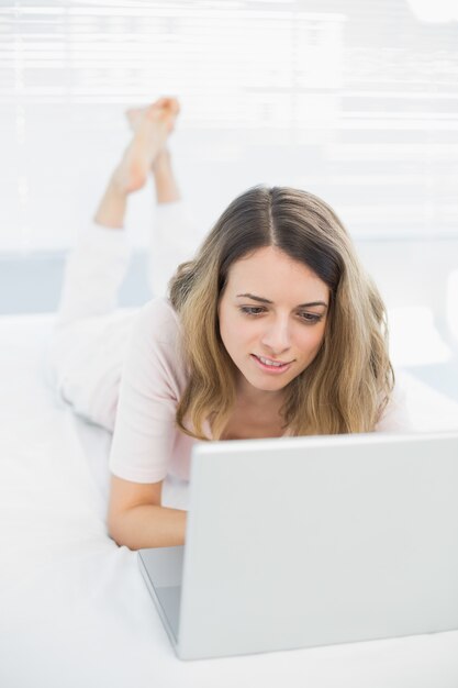 Cute young woman using her notebook lying on her bed