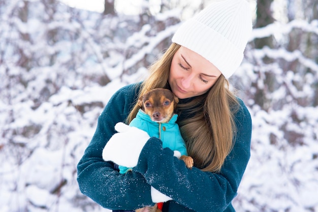 겨울에 귀여운, 젊은 여자는 추위에 그의 개를 따뜻하게 합니다. 눈 속에서 치와와 애완동물을 안고 있는 소녀가 얼어붙었습니다.