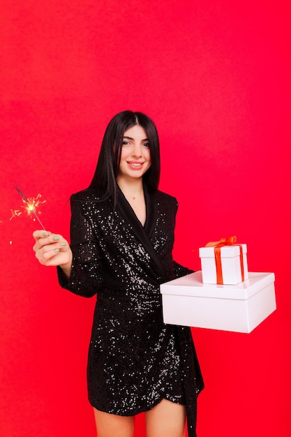 Cute young woman with Christmas gifts The model holds sparklers on a red background