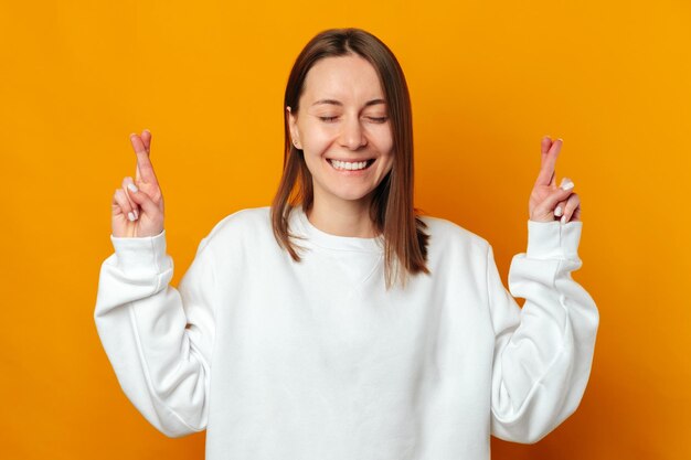 Cute young woman with eyes closed has crossed her fingers for a big wish