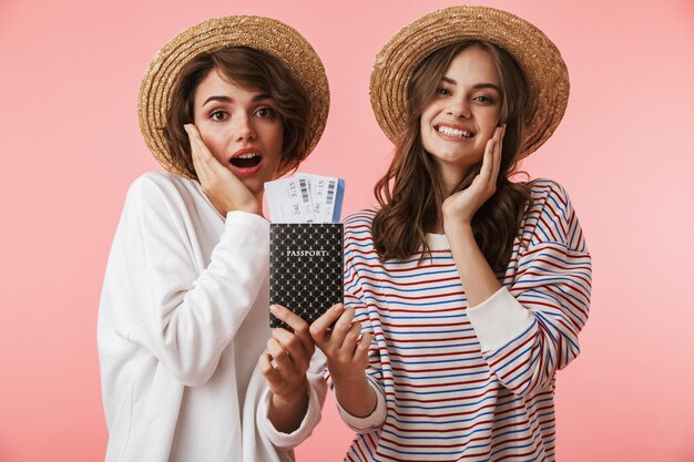 Cute young women friends posing isolated holding tickets and passport.