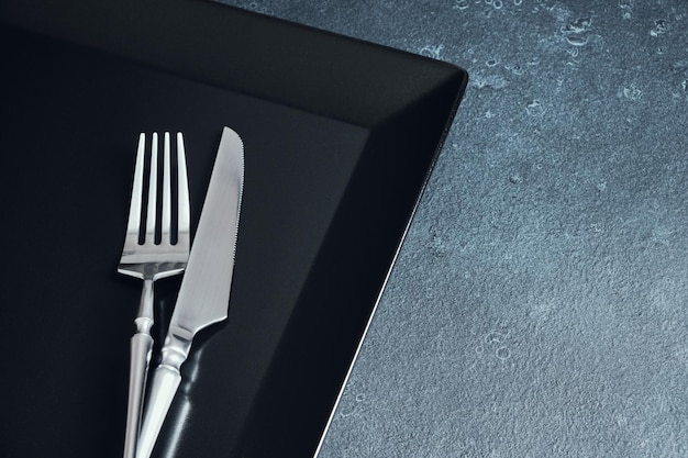 어두운 질감의 배경 테이블 설정에 있는 칼붙이와 검은색 네모난 접시