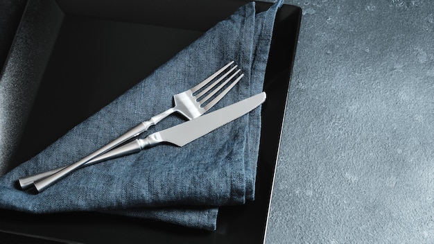 Cutlery and blue linen napkin on a black square dish table setting