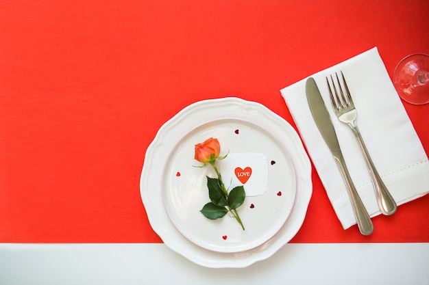 Cutlery, rose and card on red background